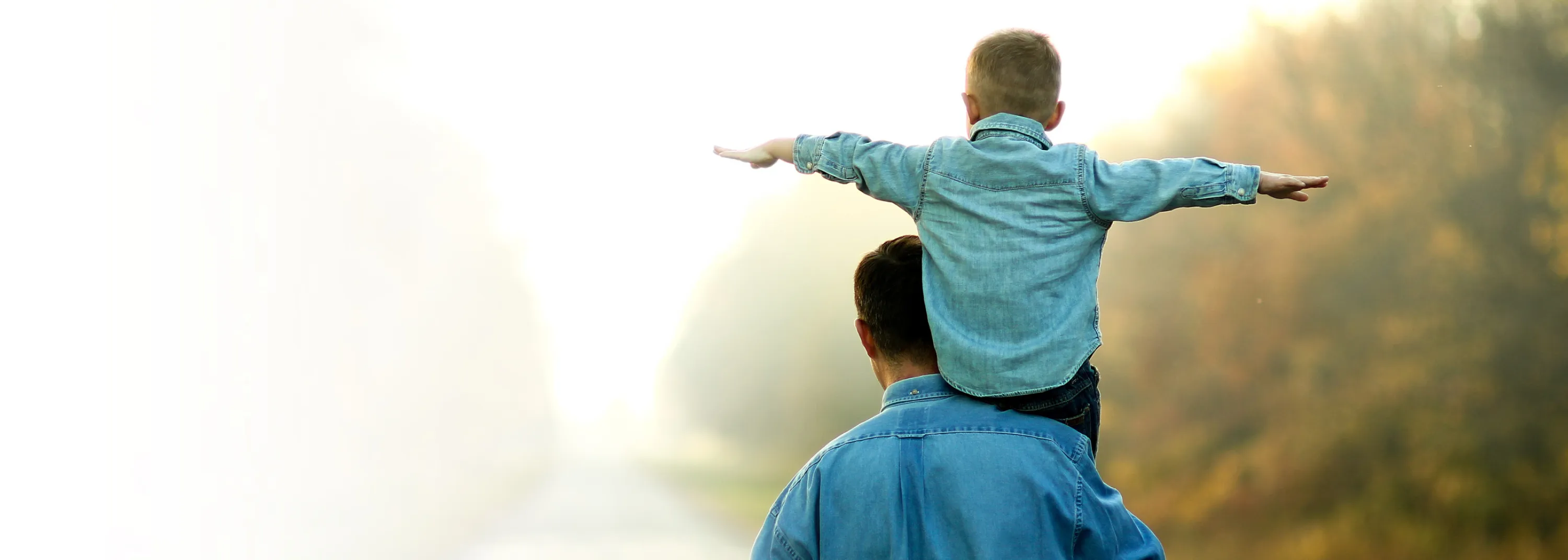 Ein Vater trägt sein Sohn auf den Schultern und sie stehen beide auf einem Kiesweg